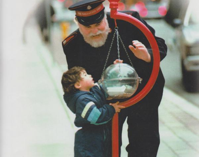 Corps Officer in uniform helping young child put money in the Salvation Army kettle